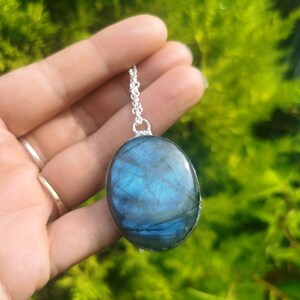 May include: A silver chain necklace with a large oval-shaped pendant made of blue labradorite gemstone.