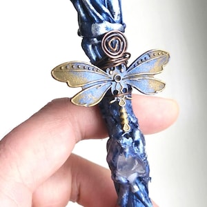 May include: A handcrafted blue wand with a clear crystal orb at the top. The wand features a dragonfly charm with gold and blue wings, and a copper wire spiral. A unique fantasy item.