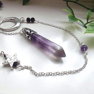 Op de afbeelding: Een zilveren ketting met een halve maan bedel, een ster bedel en een paarse amethist kristallen slinger. De ketting is versierd met kleine paarse kralen.