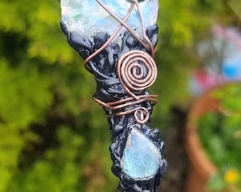 May include: A black wand with a crescent moon shaped iridescent glass piece at the top, wrapped in copper wire. A smaller iridescent glass piece is below the moon, also wrapped in copper wire.