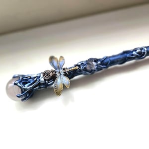 May include: A handcrafted wand with a blue and silver finish, adorned with a dragonfly charm and a rose quartz crystal sphere at the tip. The wand is approximately 12 inches long, perfect for cosplay or fantasy enthusiasts.