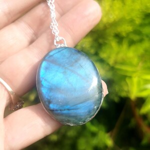 May include: A silver chain necklace with a large oval-shaped pendant made of blue labradorite gemstone.