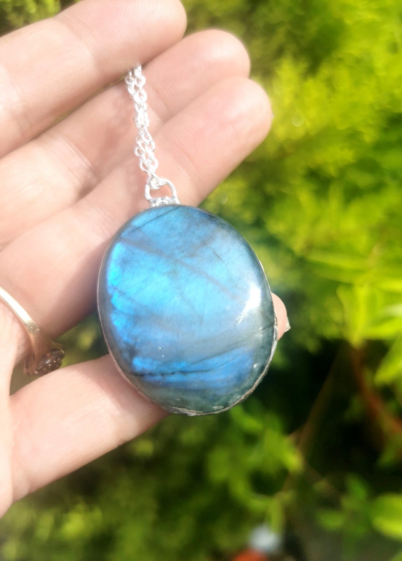 May include: A silver chain necklace with a large oval-shaped pendant made of blue labradorite gemstone.