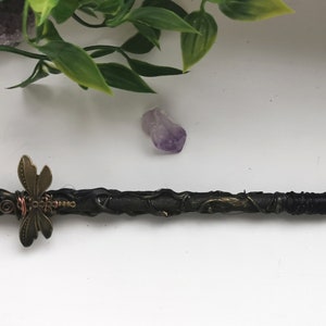 May include: A black wand with a purple amethyst crystal at the tip, wrapped in black wire and decorated with a bronze dragonfly charm.
