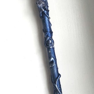 May include: A handcrafted blue and silver wand with a crystal at the base and a crystal ball at the top. A dragonfly charm is affixed to the wand's center. The wand is approximately 12 inches long.