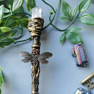 May include: A wand with a clear crystal at the top, a dragonfly charm, and a brown and gold painted finish.