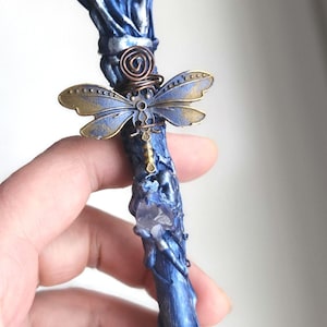 May include: A handcrafted blue wand with a clear crystal orb at the top. The wand features a dragonfly charm and a spiral design. The wand is approximately 10 inches long.