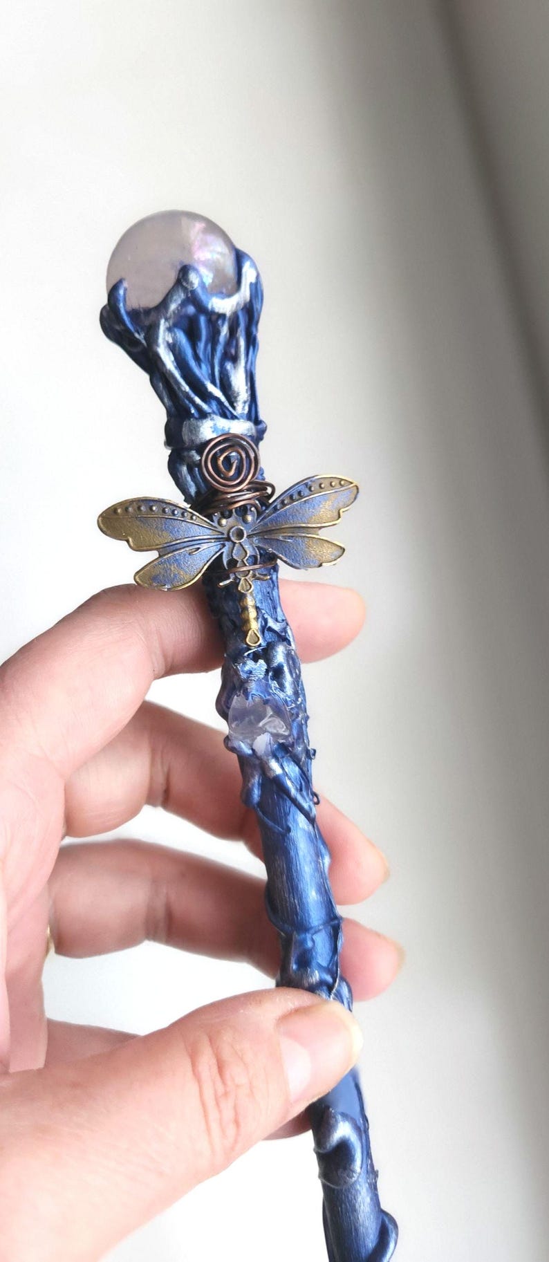 May include: A handcrafted blue wand with a clear crystal orb at the top. The wand features a dragonfly charm and a spiral design. The wand is approximately 10 inches long.