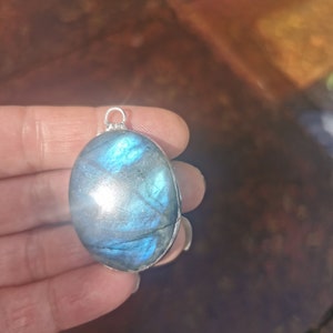 May include: A silver pendant with a large oval-shaped blue labradorite gemstone. The stone has a shimmering iridescent effect.