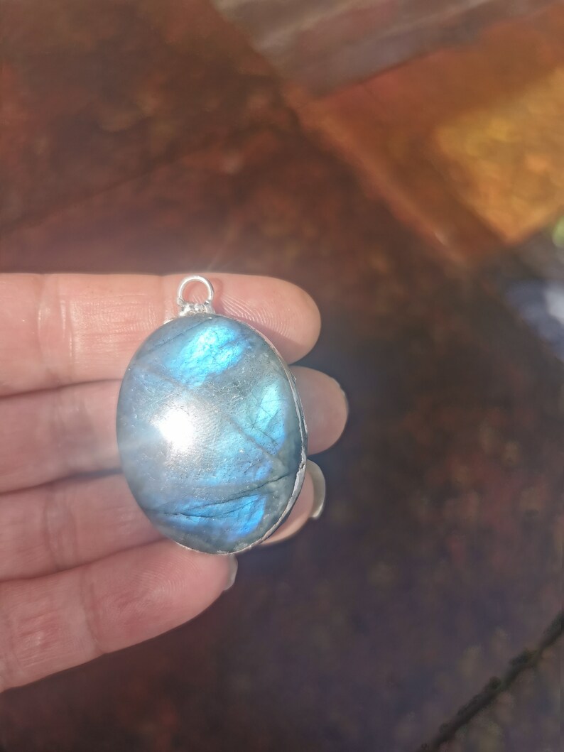 May include: A silver pendant with a large oval-shaped blue labradorite gemstone. The stone has a shimmering iridescent effect.