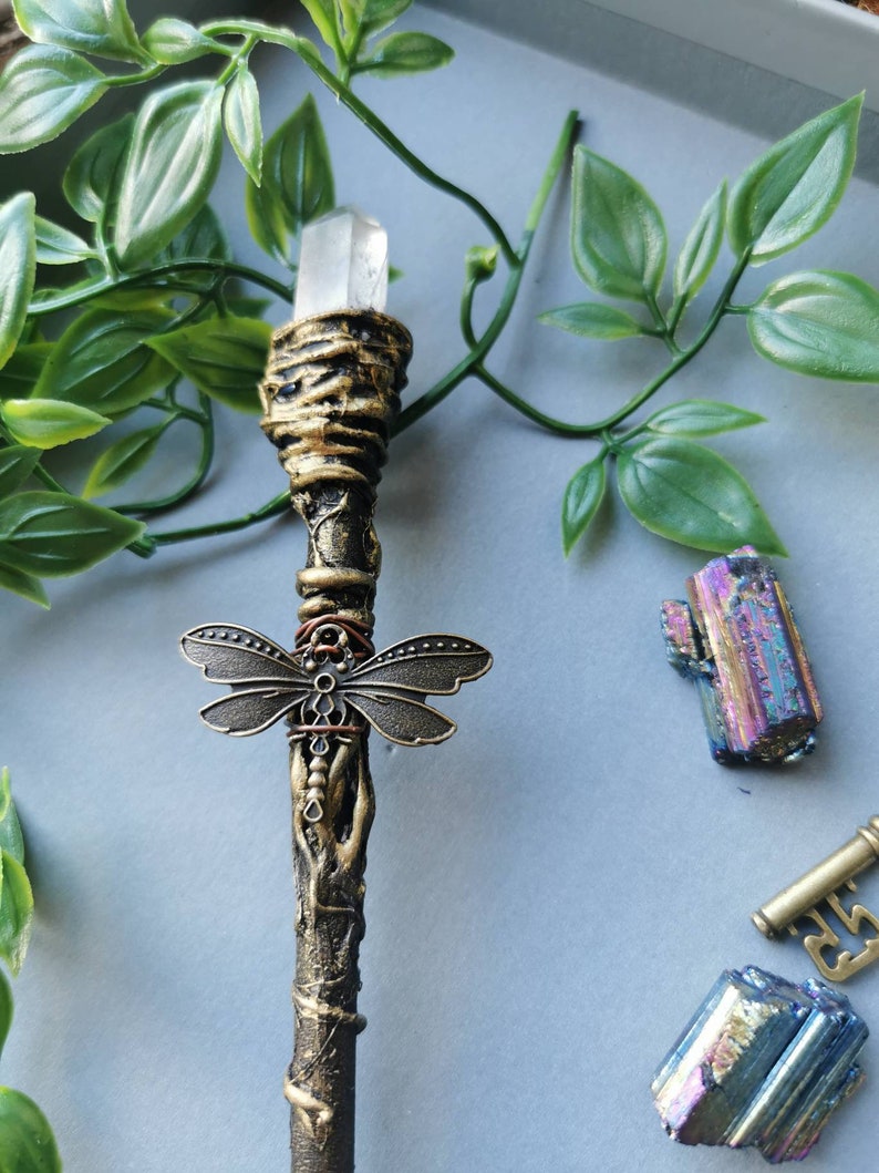 May include: A wand with a clear crystal at the top, a dragonfly charm, and a brown and gold painted finish.