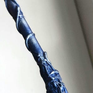 May include: A dark blue wand with silver accents and a clear crystal tip. The wand has a textured, organic design with swirling patterns and a detailed handle. The crystal is faceted and reflects light.