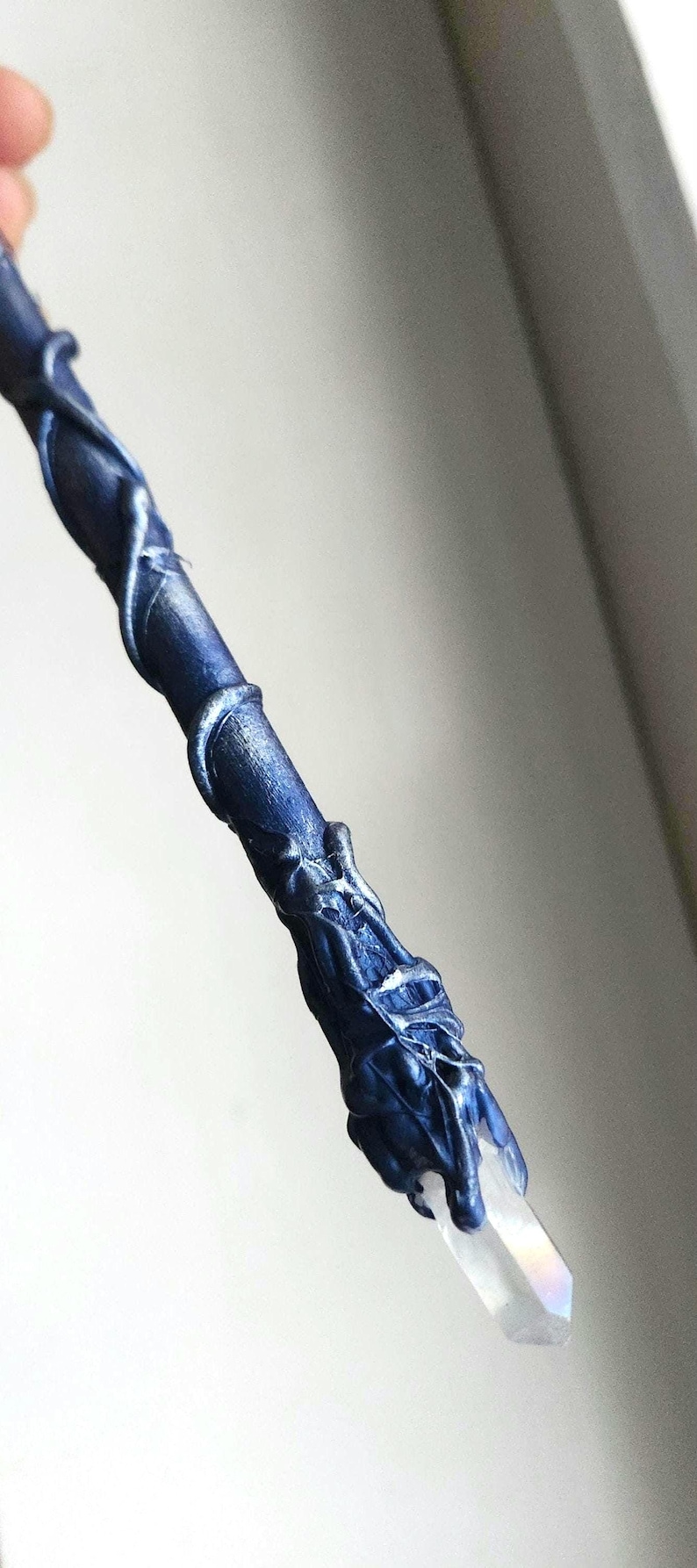 May include: A dark blue wand with silver accents and a clear crystal tip. The wand has a textured, organic design with swirling patterns and a detailed handle. The crystal is faceted and reflects light.