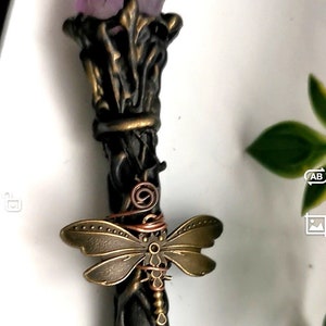 May include: A black wand with a purple amethyst crystal at the top. The wand is decorated with a bronze dragonfly and copper wire.