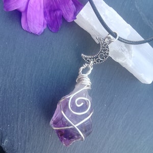 May include: A purple amethyst crystal wrapped in silver wire, hanging from a black cord with a silver crescent moon charm.