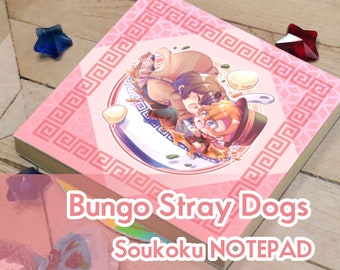 May include: Pink notepad with a decorative border and the text "Bungo Stray Dogs Soukoku NOTEPAD". The notepad features an anime-style illustration of two characters. The background includes decorative star-shaped objects.