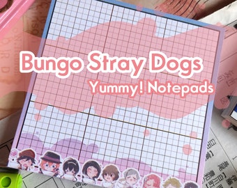 May include: Square notepad with a grid pattern, featuring the text "Bungo Stray Dogs Yummy! Notepads." The design includes a pink and purple watercolor wash and character illustrations along the bottom edge.