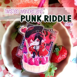 Può includere: Un ciondolo in acrilico trasparente con un personaggio dei cartoni animati in rosso e nero, che tiene un cucchiaio d'oro sopra un dessert alle fragole. Il ciondolo ha il testo "PUNK RIDDLE charm" e "TWISTED WONDERLAND".