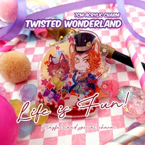 Op de afbeelding: Een 7 cm acryl bedel met twee anime-stijl personages uit "Twisted Wonderland". De bedel heeft een kleurrijk ontwerp met de tekst "Life is Fun!" en "Playful land special charm". De achtergrond is een roze en wit geruit patroon.