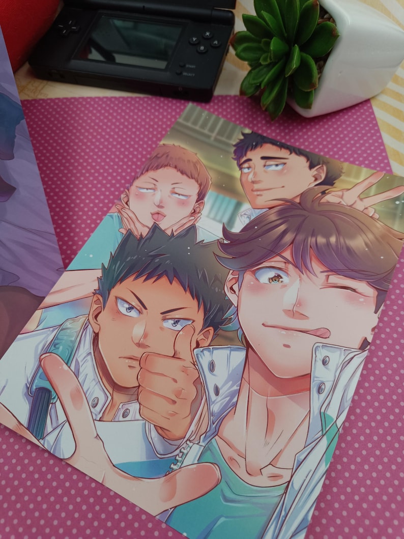 K&ouml;nnte beinhalten: Ein farbenfroher Anime-Print mit vier m&auml;nnlichen Charakteren in einer Gruppenpose. Ein Charakter hebt den Daumen, ein anderer zwinkert. Das Kunstwerk hat eine lebendige Farbpalette und detaillierte Gesichtsausdr&uuml;cke. Im Hintergrund ist eine schwarze Handheld-Konsole zu sehen.
