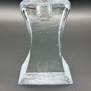 May include: Clear glass candle holder with a flared top and a rectangular base. The label reads "BLENKO HANDCRAFT Made in USA". The glass has a textured appearance and is transparent.