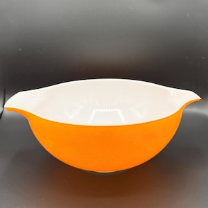 May include: An orange and white mixing bowl with a floral pattern on the exterior. The bowl has a rounded shape with two handles on either side. The interior is white, and the exterior is a vibrant orange.