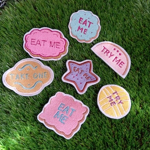 Può includere: Sette toppe ricamate da stirare in varie forme e colori con il testo "Eat Me", "Try Me" e "Take One".