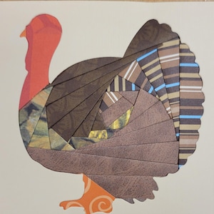 May include: A Thanksgiving-themed greeting card featuring a turkey illustration. The turkey is composed of various patterned paper pieces in shades of brown, orange, and blue. The background is a light beige color.