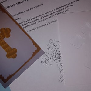 May include: A white card with a cross shape drawn on it. The cross is divided into sections with numbers written inside each section. The card is next to a purple card with a gold cross on it.