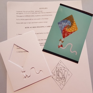 May include: A white cardstock template for a kite-shaped folding card. The template has a cut-out shape of a kite with a tail. The card is labeled with numbers 1 through 13. The instructions for the card are printed on a separate sheet of paper.