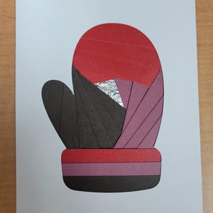 May include: A paper art mitten design. The mitten is constructed from sections of red, black, and purple paper, with a silver foil detail. The artwork is set against a white background, creating a striking contrast.