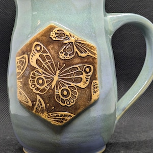 May include: A blue ceramic mug with a hexagonal design featuring a brown butterfly and other floral patterns.