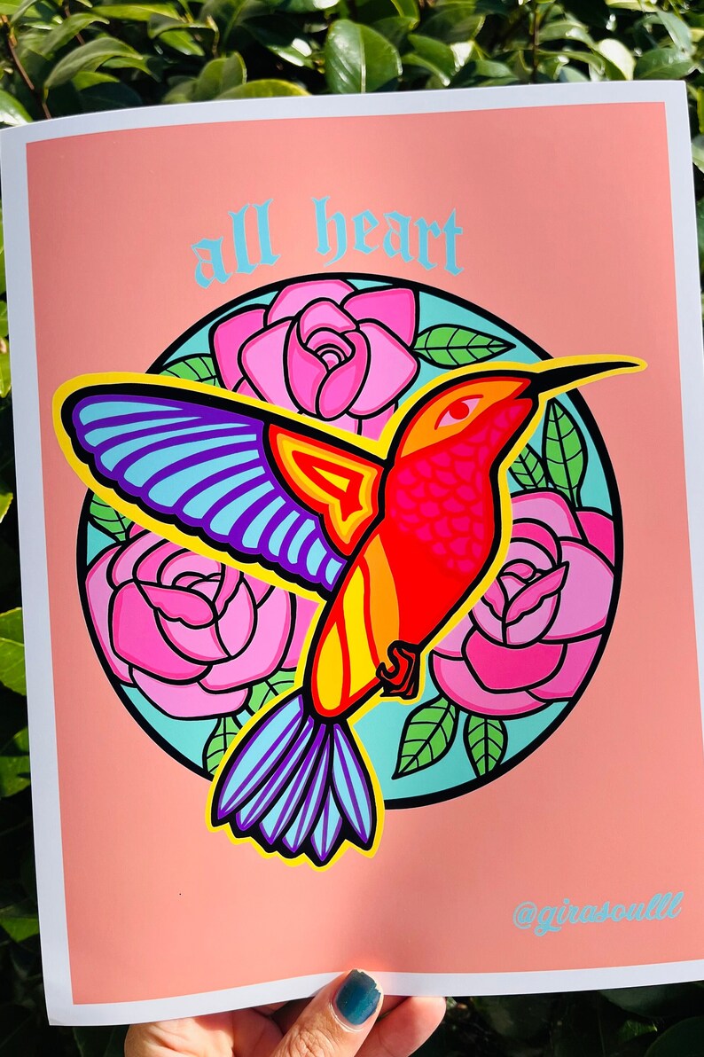 8.5x11 digital illustration featuring a fiery hummingbird in oranges and yellows with a halo of pink roses behind them and the words ‘all heart’ on top of the halo in blue and old English type. The background is a blush orange tone.