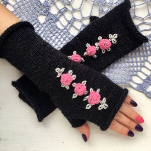 May include: Black knitted fingerless gloves with pink flower embroidery.