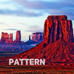Op de afbeelding: Een panoramisch uitzicht op rode rotsformaties in een woestijnlandschap. De lucht is een levendig blauw met roze en paarse tinten. De rotsformaties zijn hoog en slank, met scherpe randen. Het landschap is kaal en droog, met een paar verspreide planten.