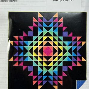 May include: A quilt kit featuring a colorful geometric pattern with a black background. The kit includes grunge fabrics and is designed for an advanced beginner. The quilt size is 64 inches by 64 inches.
