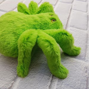 Pode incluir: Um brinquedo de aranha de pel&uacute;cia verde brilhante com pernas grandes e felpudas. A aranha tem olhos pretos e uma textura macia e fofa.