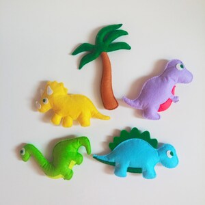 May include: Five felt dinosaur toys, including a green dinosaur, a blue dinosaur, a yellow dinosaur, a purple dinosaur, and a green palm tree.
