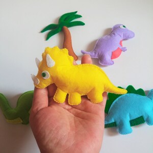 May include: A set of felt dinosaur toys, including a yellow triceratops, a purple tyrannosaurus rex, a blue stegosaurus, and a green brachiosaurus. The dinosaurs are all hand-sewn and have embroidered details.