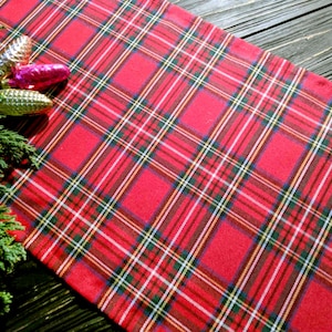 May include: Red and green tartan table runner with a festive Christmas theme. The runner is decorated with three small baubles.