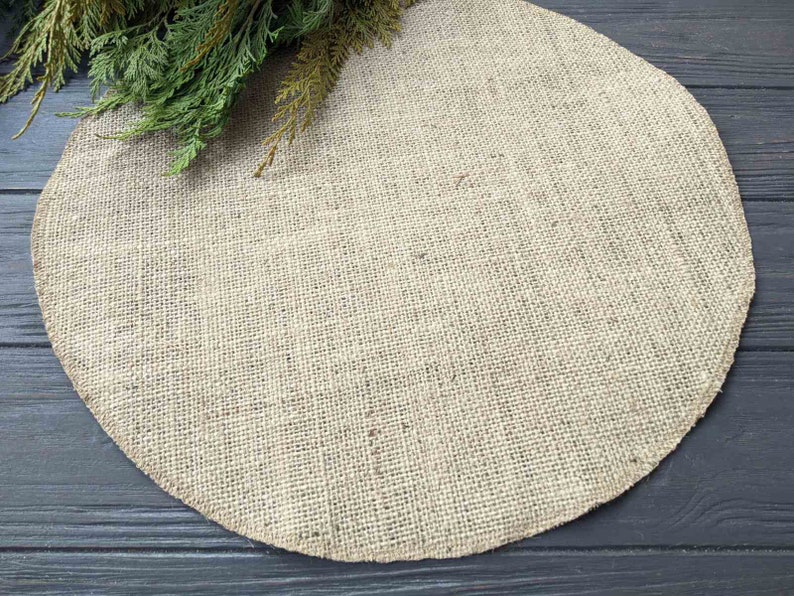 May include: A round, beige burlap placemat on a dark wood surface.