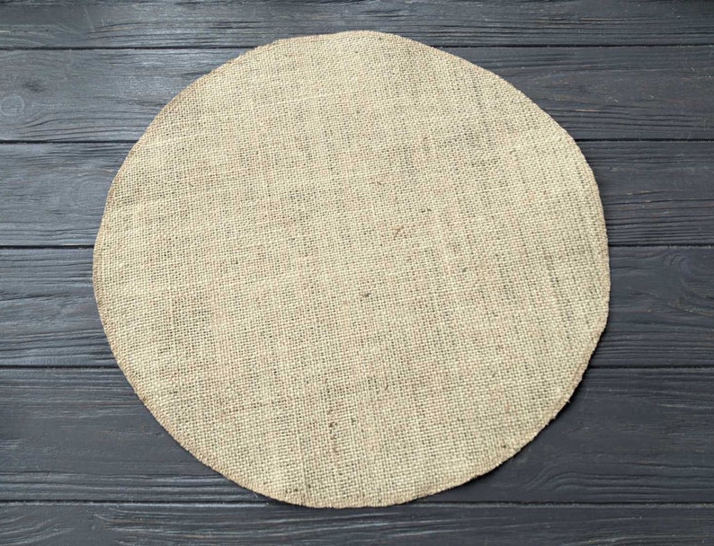 May include: A round, beige burlap placemat on a dark wood surface.