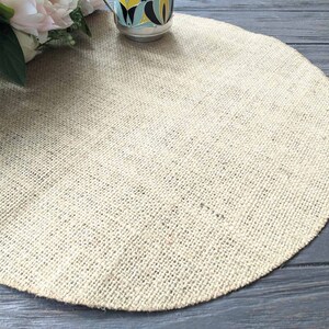 May include: A round, beige burlap placemat on a dark wood surface.