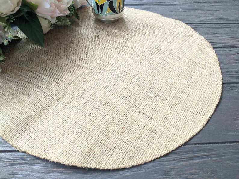 May include: A round, beige burlap placemat on a dark wood surface.