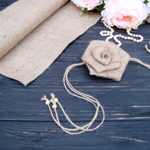 Pu&ograve; includere: Un fiore di juta con una collana di perle e perline di legno su uno sfondo di legno scuro.