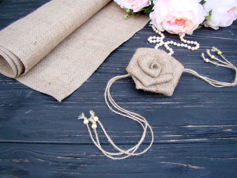 Pu&ograve; includere: Un fiore di juta con una collana di perle e perline di legno su uno sfondo di legno scuro.