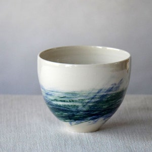 May include: A white ceramic bowl with a blue and green abstract design. The bowl is round and has a smooth, glossy finish.