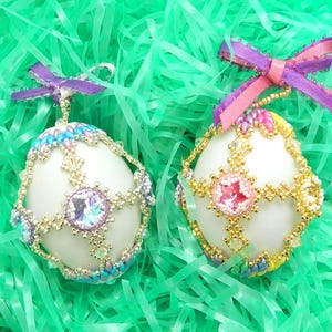 Może przedstawiać: Dwa białe, koralikowe jajka wielkanocne ozdobione kolorowymi koralikami i kryształkami. Jajka leżą na zielonym, posiekanym papierze.