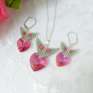 May include: A pink crystal heart pendant necklace and matching earrings with a silver chain and beaded wings in shades of green, pink, and silver.