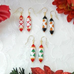May include: Three pairs of cylindrical beaded drop earrings with gold-tone hooks. One pair features red hearts on white, one pair has orange pumpkins on white with black ends, and one pair displays green Christmas trees on white with red ends.